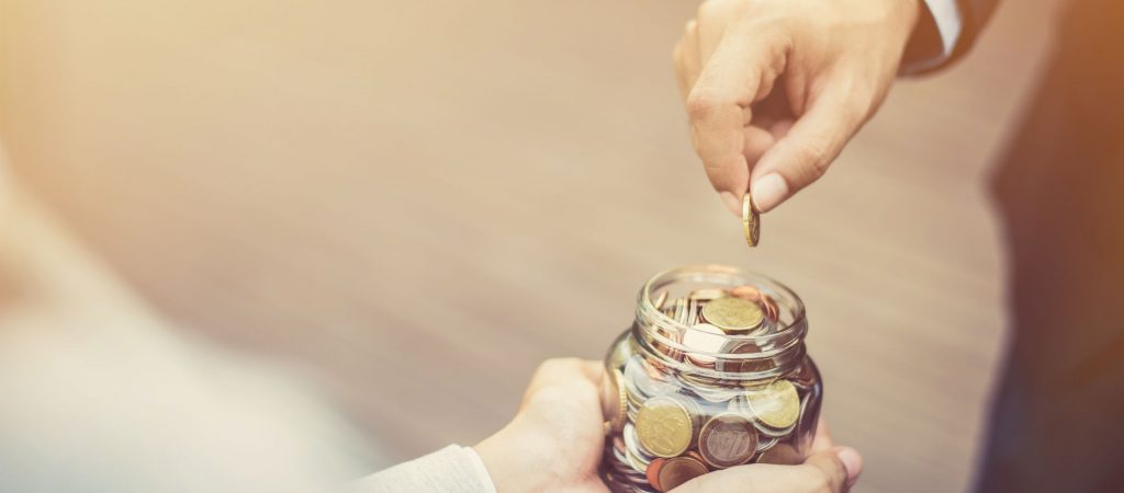 Businessman hand putting money (coin) in the glass jar held by a woman, vintage tone effect